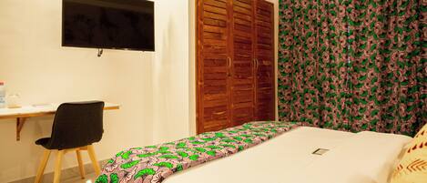 A bedroom with a bed, a desk with a chair, a television, a wardrobe, and a curtain.