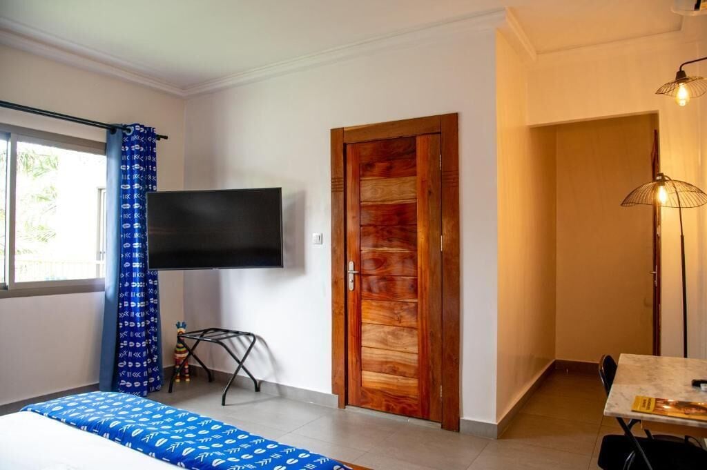 A bedroom with a bed, a TV, a wooden door, and a dining area with a table and chairs.