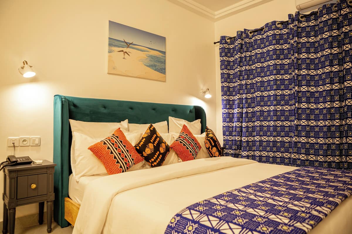 Una cama con ropa de cama estampada, una mesita de noche con un teléfono y un cuadro colgado en la pared.