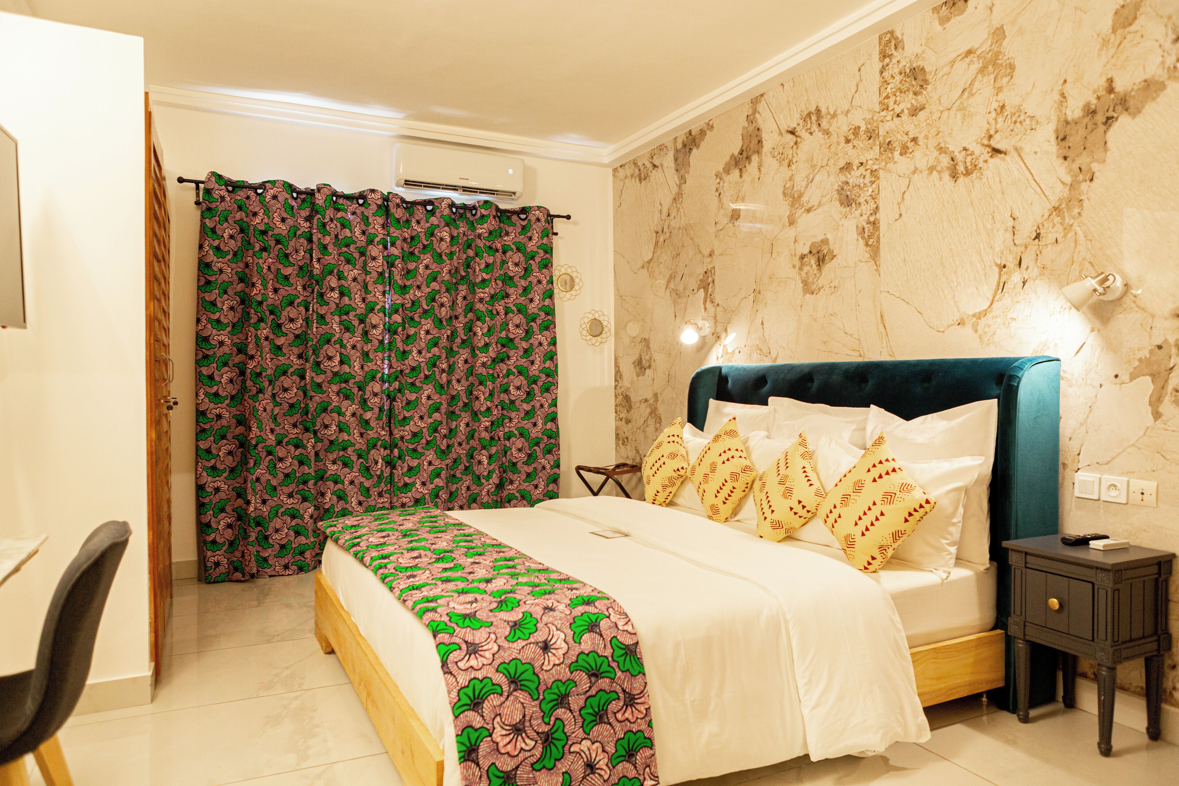 A bedroom with a bed, a desk, a chair, a nightstand, and a curtain.