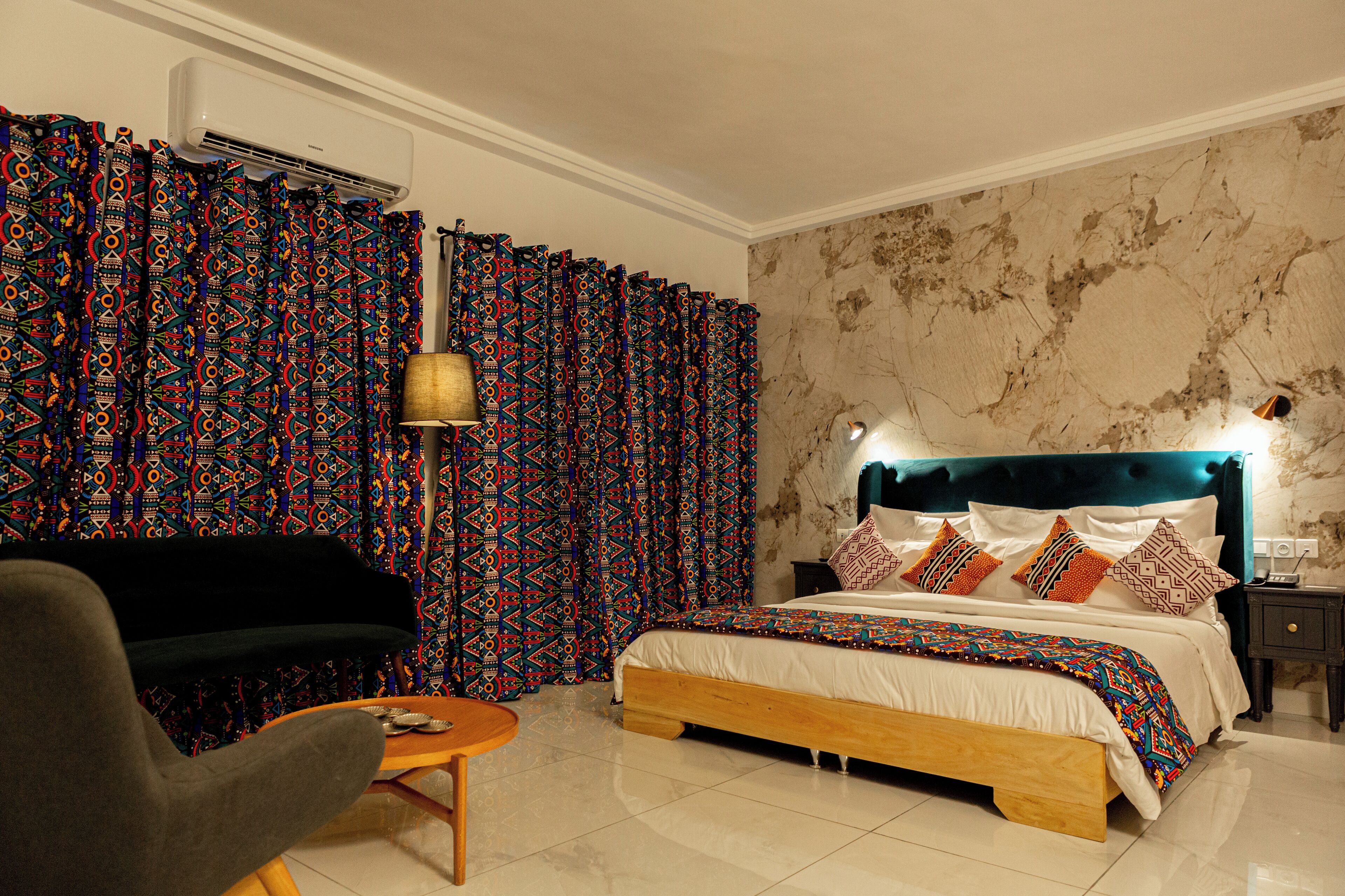 Un dormitorio con cama, cortinas, una silla, una lámpara y una mesita de noche.