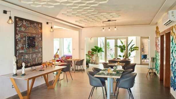 A spacious dining area with modern furniture, a large decorative wall, and a ceiling with geometric patterns. - LE KARE EBENE (Cotonou)