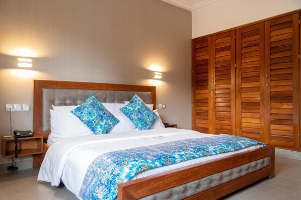 A hotel room with a large bed, wooden wardrobe, and two bedside lamps.