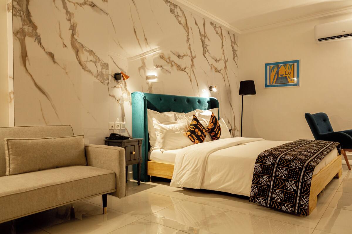 Un dormitorio con una cama, un sofá, una mesita de noche, una lámpara y una silla.