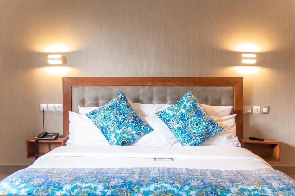 A hotel room with a bed, two patterned pillows, a bedside phone, and a bedside table.