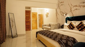 A bedroom with a bed, a nightstand, a lamp, a sofa, and a patterned curtain. - LE KARE EBENE (Cotonou)