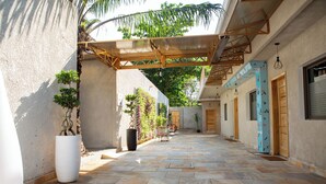A covered outdoor corridor with stone flooring, potted plants, and wooden doors. - LE KARE EBENE (Cotonou)