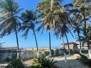 A beachside view with palm trees, a white fence, and a building with a red roof. - U-go Faro Tequendema (Cartagena)
