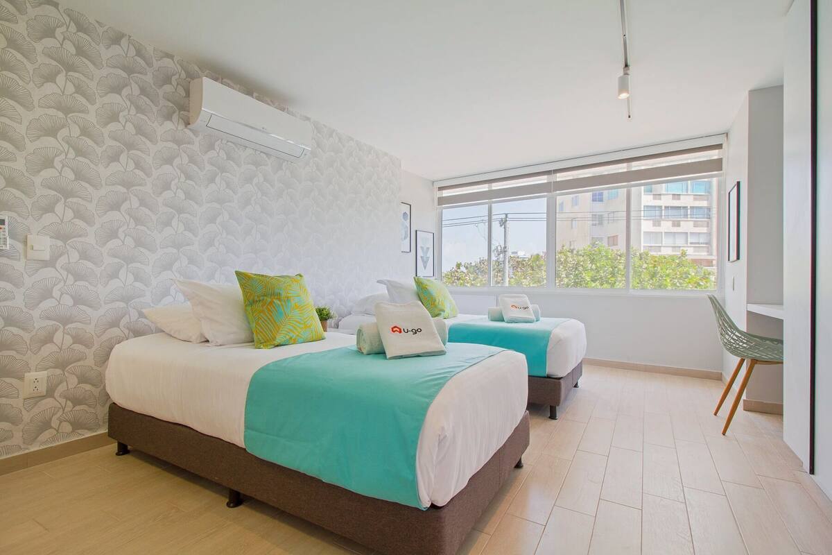 A modern hotel room with two beds, a large window, and a view of the city.