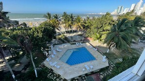 A rooftop pool with lounge chairs, surrounded by palm trees and a view of the ocean and city skyline. - U-go Faro Tequendema (Cartagena)