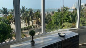 A room with a large window overlooking a beach and cityscape, a small potted plant, and a wooden table with a bowl. - U-go Faro Tequendema (Cartagena)