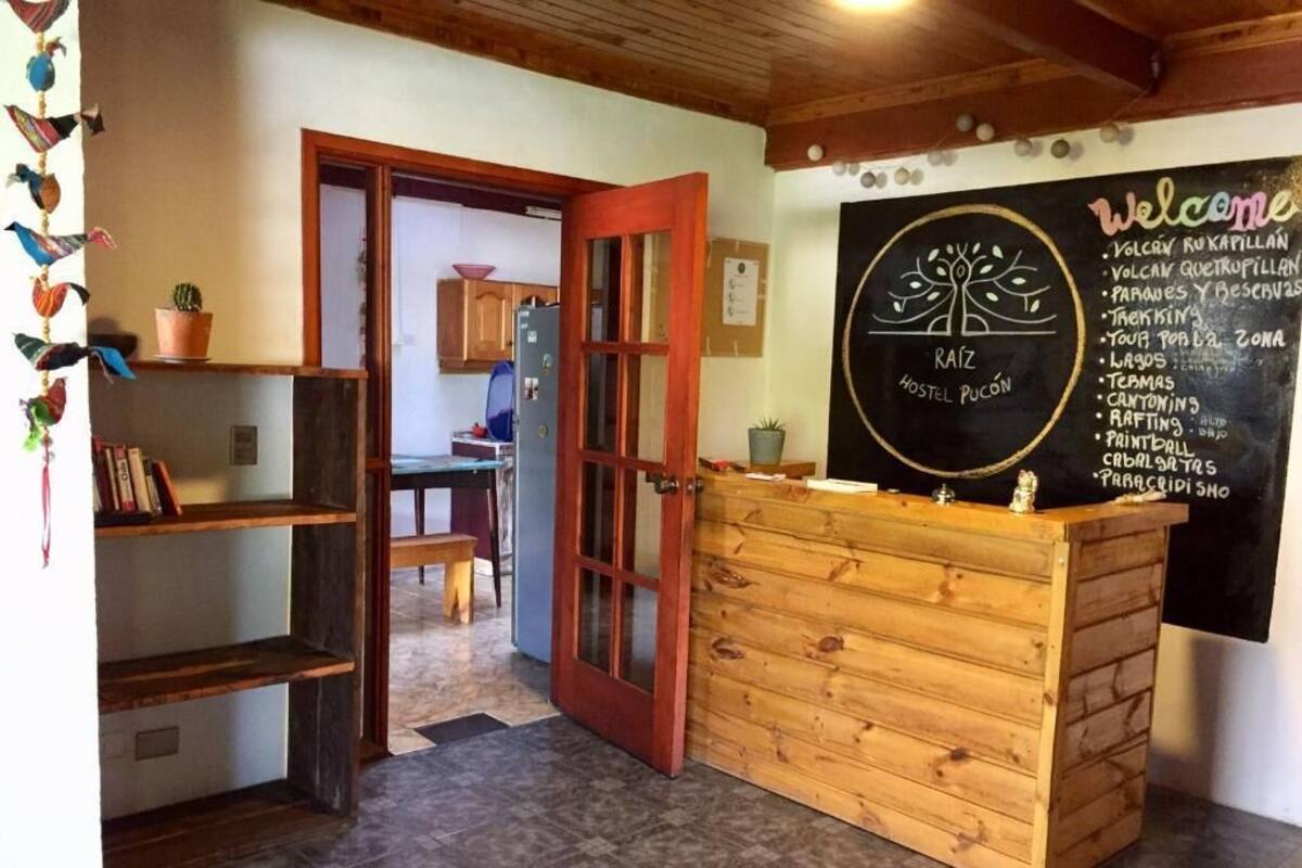 Ein Hostel-Empfangsbereich mit einem Holztresen, einer Kreidetafel mit Speisekarte und einer Tür zu einem Essbereich.