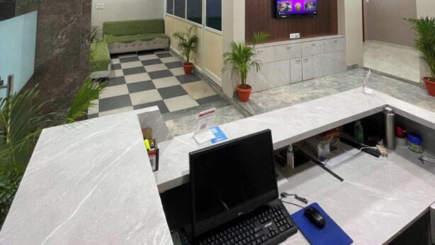 Ein modernes Büro mit Schachbrettmuster-Boden, einem Schreibtisch mit Laptop, einem Deckenventilator und einem Wand-Fernseher.