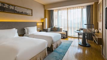 A hotel room with two beds, a desk, a chair, a table, and a large window with curtains.