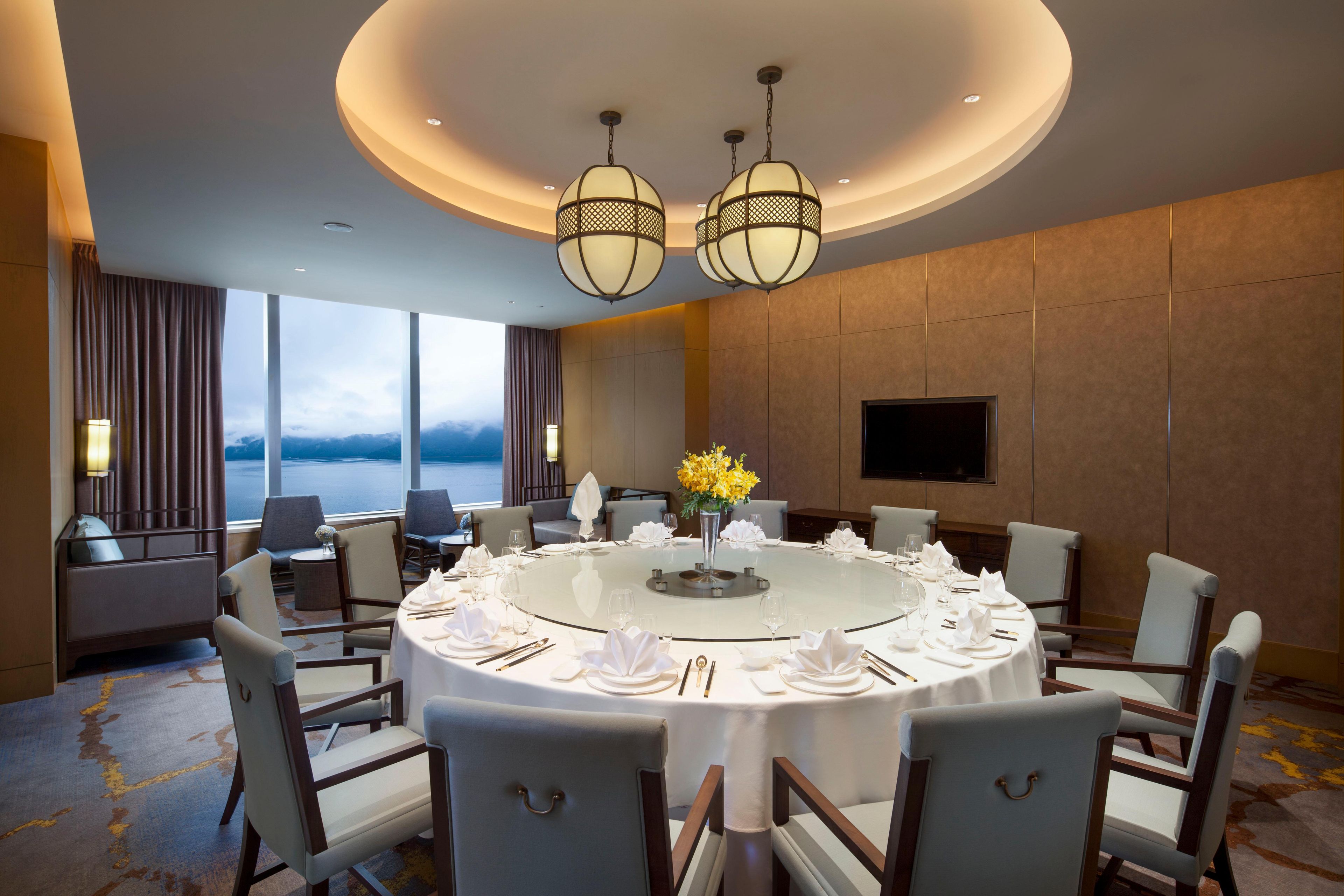 A round dining table set for six with white linens and a vase of yellow flowers, surrounded by chairs with wooden frames and cushioned seats.