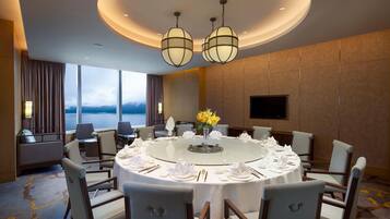 A round dining table set for six with white linens and a vase of yellow flowers, surrounded by chairs with wooden frames and cushioned seats.
