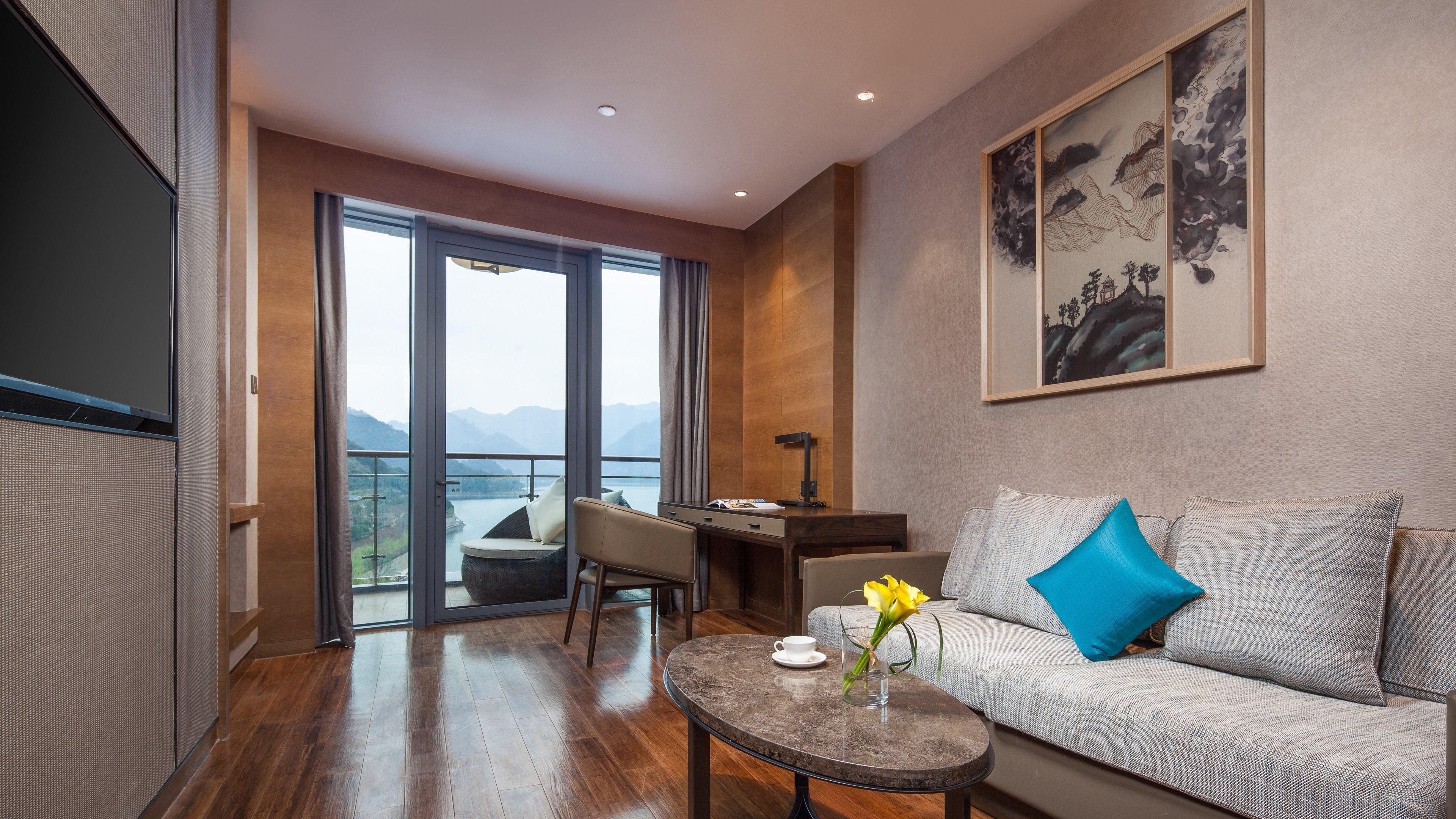 Una sala de estar moderna con un sofá, una mesa de centro y un escritorio, un ventanal con vistas a montañas y un cuadro en la pared.