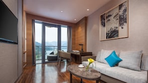 A modern living room with a sofa, coffee table, and desk, a large window with a view of mountains, and a painting on the wall. - Crowne Plaza Hangzhou Thousand Island Lake (Hangzhou)