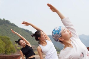 Tres personas realizan una postura de yoga al aire libre, con montañas al fondo.