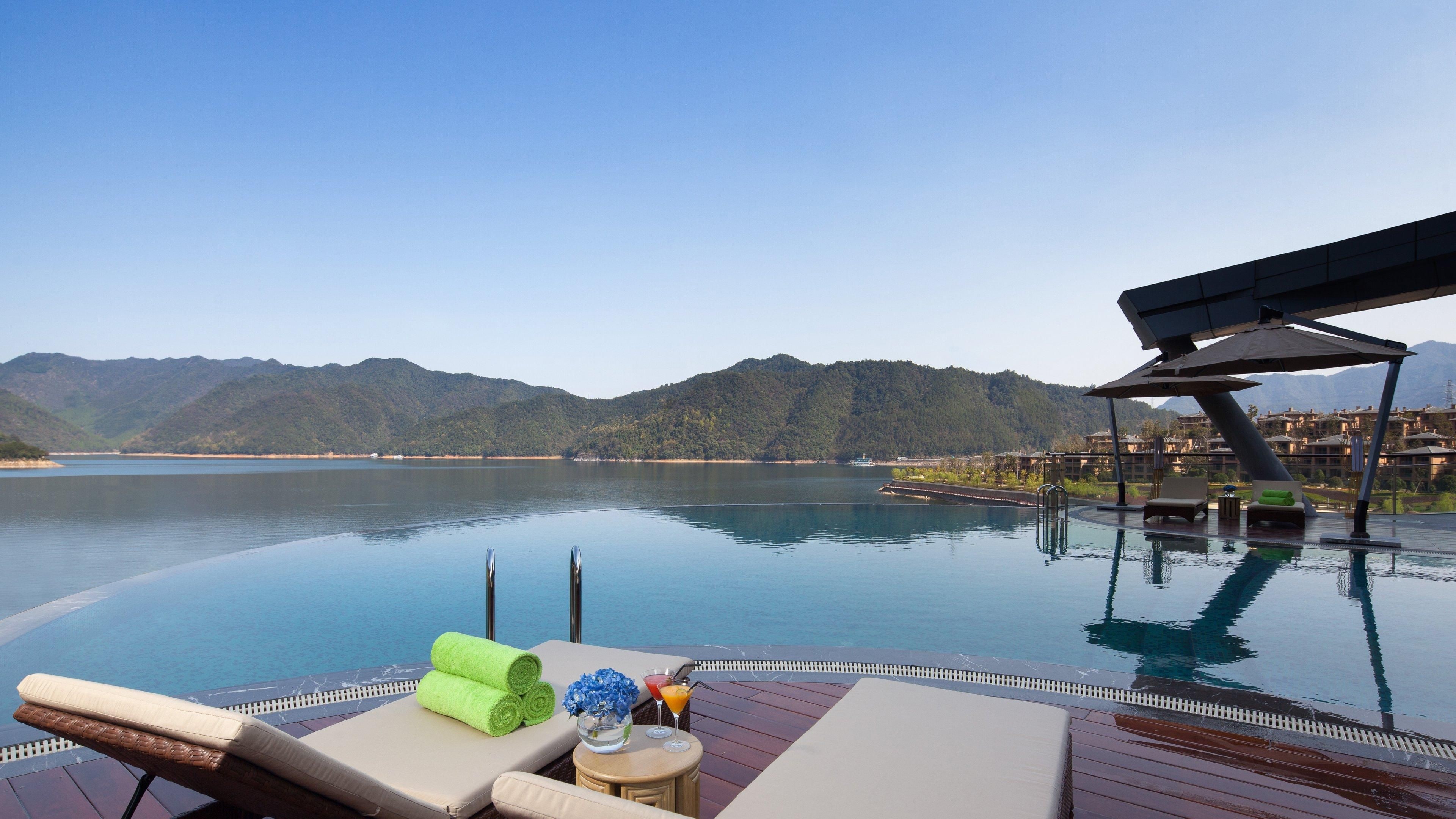 Ein Infinity-Pool mit Liegestühlen, einem Tisch mit Getränk und Blick auf die Berge.