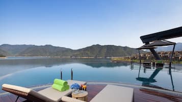 Ein Infinity-Pool mit Liegestühlen, einem Tisch mit Getränk und Blick auf die Berge.