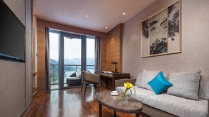 A modern living room with a sofa, coffee table, and desk, a large window with a view of mountains, and a painting on the wall.