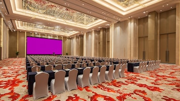 A conference room with rows of tables and chairs, a large screen, and a patterned carpet.