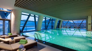 An indoor swimming pool with lounge areas, large windows, and a view of mountains. - Crowne Plaza Hangzhou Thousand Island Lake (Hangzhou)