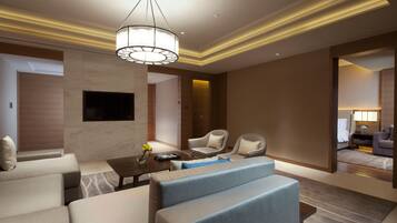 A modern hotel room with a sofa set, a coffee table, a TV mounted on the wall, and a large mirror reflecting the room.