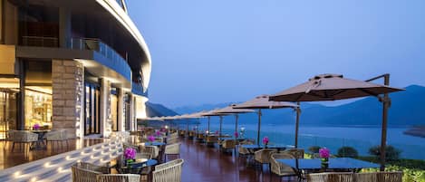 A waterfront restaurant with outdoor seating, tables, chairs, and umbrellas.