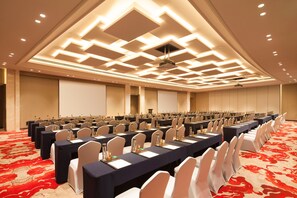 A conference room with rows of tables, chairs, and a red carpeted floor.