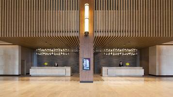 A spacious lobby with a central reception desk, wooden paneling on the walls, and a modern chandelier.