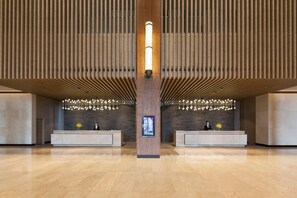 Un'ampia hall con una reception centrale, pannelli di legno sulle pareti e un moderno lampadario.