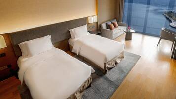 A hotel room with two beds, a sofa, a small table, and a view of a body of water.