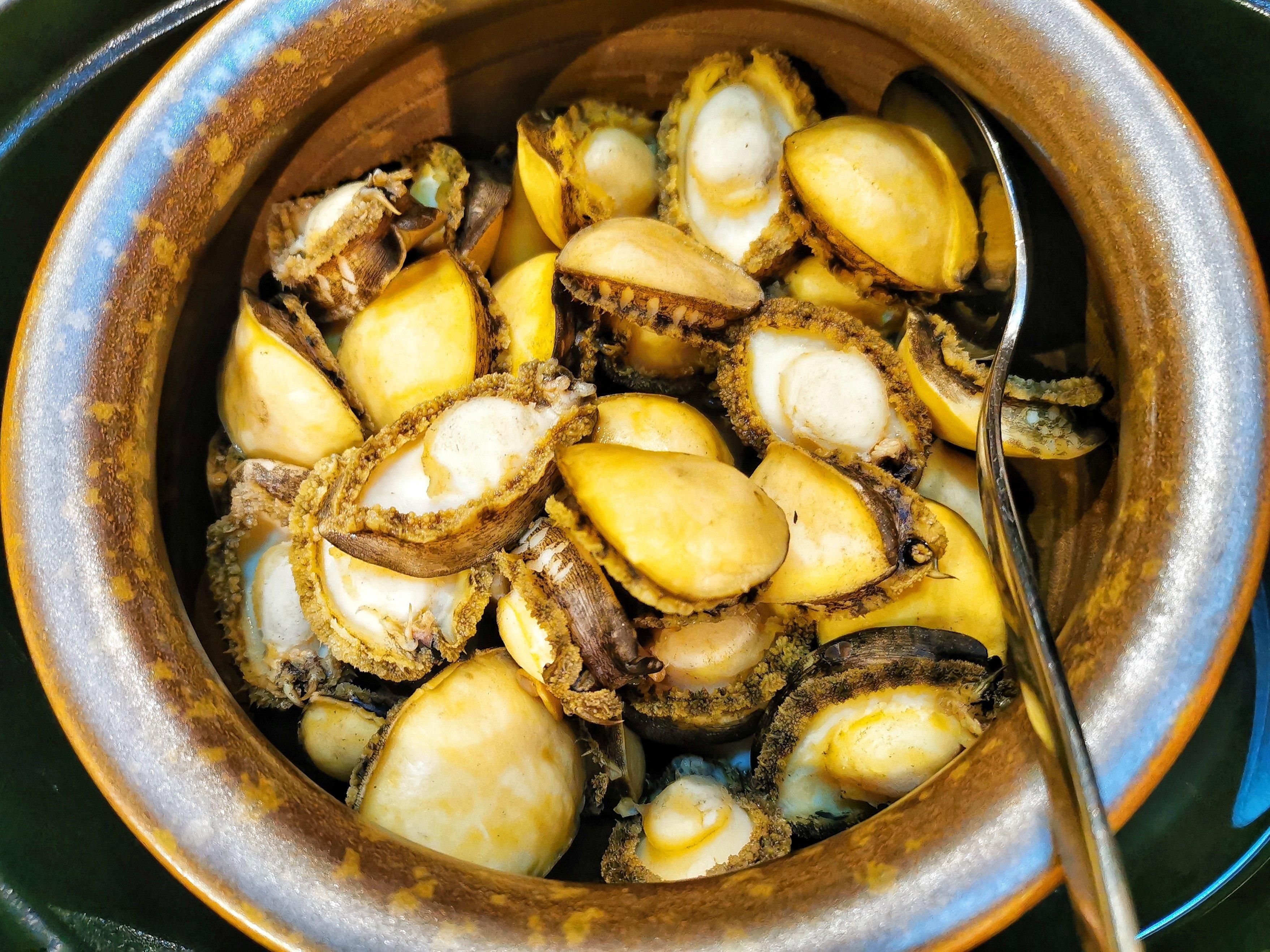 A bowl of cooked clams with a spoon.