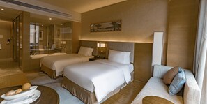 A hotel room with two beds, a sofa, a dining table with a bowl of fruit, a mirror, and a painting on the wall. - Crowne Plaza Hangzhou Thousand Island Lake (Hangzhou)
