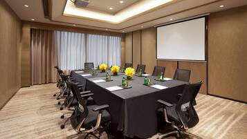 A conference room with a long table, chairs, a projector screen, and floral centerpieces.