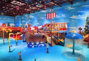 An indoor water park with a ship-themed play area, slides, and a water fountain.