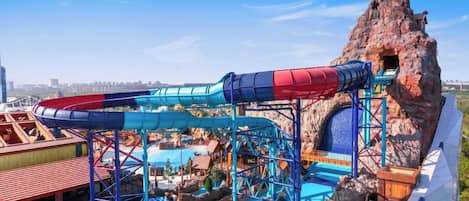 Un parque acuático con un tobogán gigante, una piscina y montañas rocosas al fondo.