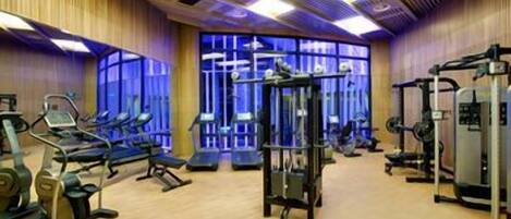 A gym with various exercise equipment, wooden floors, and large windows.