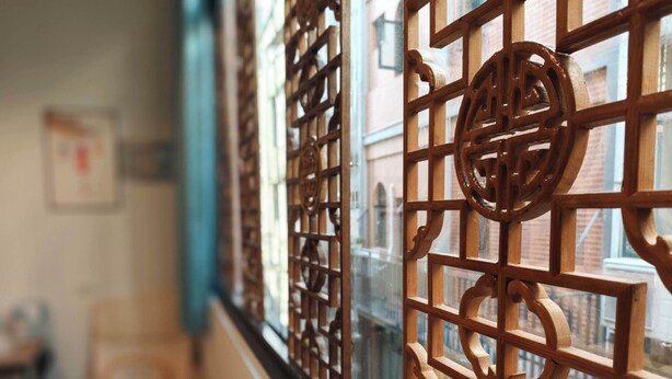 Una stanza con un divisorio in legno a griglia, una finestra vista edifici e una sedia.