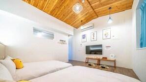 Camera d'albergo con due letti, televisione, un tavolino e un soffitto con travi in legno.