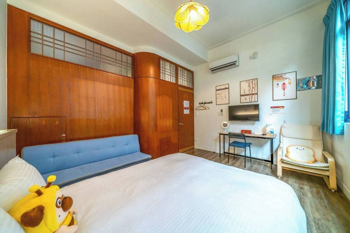 Une chambre d’hôtel avec un lit, un canapé bleu, un bureau avec une chaise, une télévision et un fauteuil décoratif orné d’un visage.