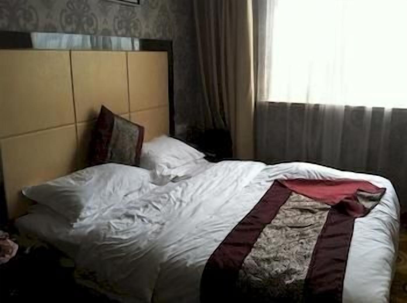 Une chambre d’hôtel avec un lit, une tête de lit, des rideaux et une fenêtre.