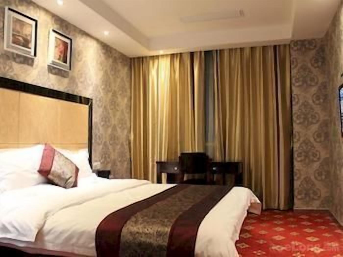 Quarto de hotel com cama, cortinas, cabeceira e uma pequena mesa.