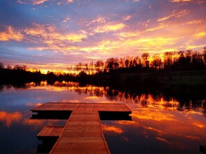 Une jetée en bois s’étendant sur une étendue d’eau calme, où se reflète le coucher de soleil.