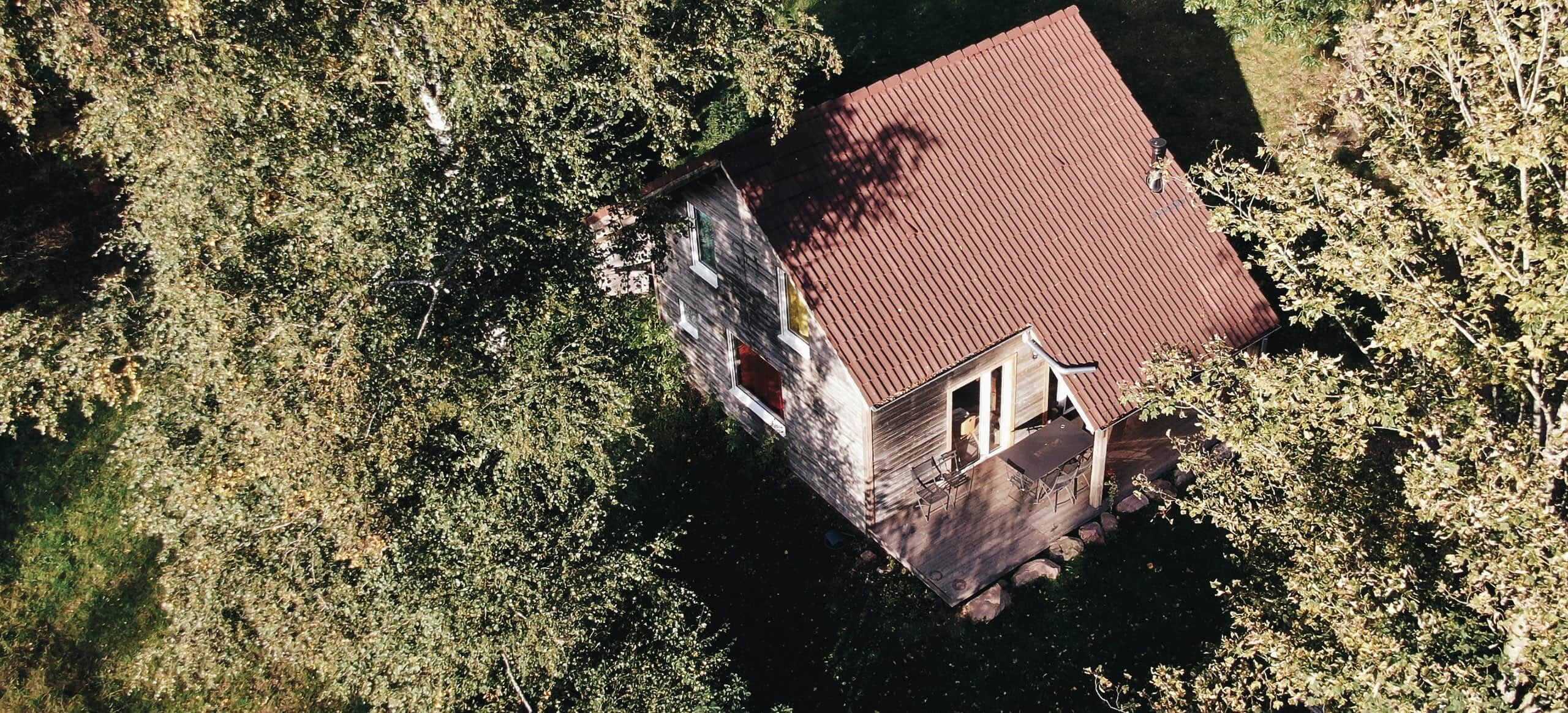 An aerial view of a house with a red roof, surrounded by dense foliage.