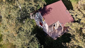 Une petite maison avec un toit rouge, entourée d’arbres denses.