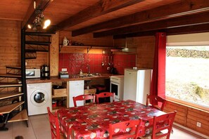 A compact kitchen with a washing machine, a microwave, a refrigerator, and a dining area with a table and chairs.