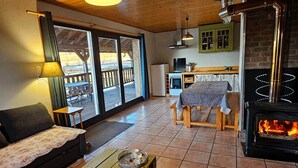 A cozy living room with a sofa, a wooden table, a fireplace, and a kitchen area with a stove. - Le Fayard - Chalet with terrace (Mélisey)